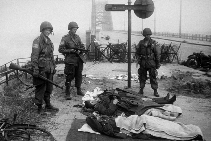 Paratroopers from the US 82nd Airborne Division, possibly from the 2nd Battalion 505 Parachute Infantry Regiment, stand guard over wounded German prisoners at the south end of the Nijmegen road bridge.