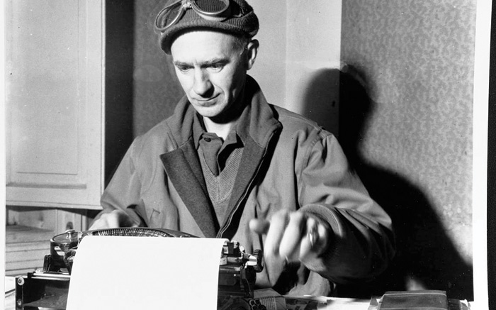 Black and white photograph of Ernie Pyle at work, sat at a typewriter.